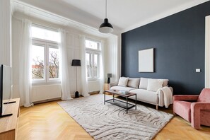 Un salon moderne avec un canapé, une table basse et un fauteuil rouge. Il y a une grande fenêtre avec des rideaux blancs, un lampadaire et un tableau accroché au mur.