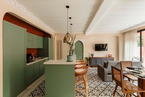 A modern kitchen with green cabinets, a central island, and a dining area with wicker chairs and a table. - New Moroccan Riad · Private Pool · Aldea Zama (Tulum)