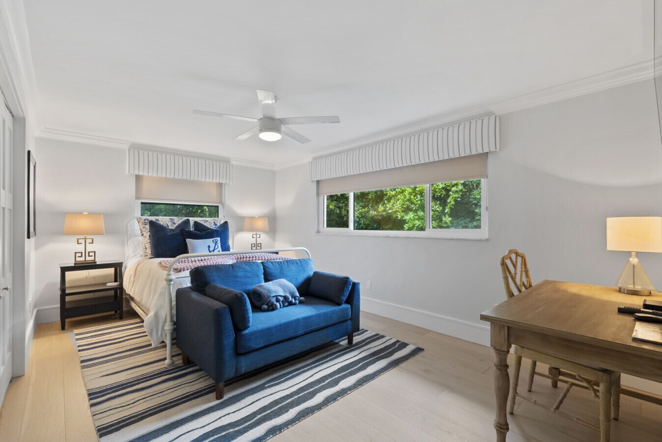 A bedroom with a bed, a blue sofa, a dining table, and a ceiling fan.