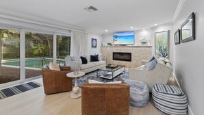 A spacious living room with a large TV, comfortable seating, a fireplace, and a view of a pool. - Fountainhead Listing Before Removing due to Annual Requirement (Naples)