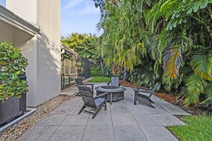Eine Terrasse im Freien mit einem runden Tisch und Stühlen, umgeben von üppiger Vegetation und Blick auf ein Gebäude.