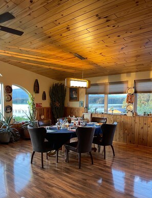 Comedor con techo y paredes de madera, una mesa dispuesta para cuatro comensales y ventanas amplias con vistas al exterior.
