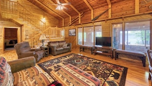 A log cabin interior with a wooden staircase, a large rug, and a television. - Cedar Point Resort and Campground (Marcell)