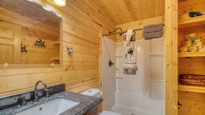 A wooden cabin bathroom with a granite sink, a toilet, and a shower. - Cedar Point Resort and Campground (Marcell)