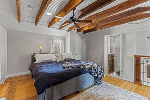 Ein Schlafzimmer mit einem großen Bett, Holzbalken, einem Deckenventilator und Blick ins Freie.
