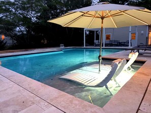Ein Schwimmbad mit Holzterrasse, Liegestühlen und Sonnenschirm.