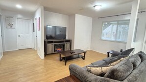 A living room with a flat-screen TV, a fireplace, a sofa, and a window with blinds. - FULLY FURNISHED – PERFECT FOR SHORT-TERM OR LONG-TERM RENTALS 
From Jan 1, 2026 (Maple Ridge)