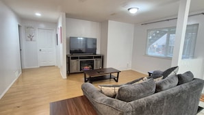 A living room with a grey sofa, a wooden coffee table, a flat-screen TV on a wooden stand, and a fireplace. - FULLY FURNISHED – PERFECT FOR SHORT-TERM OR LONG-TERM RENTALS 
From Jan 1, 2026 (Maple Ridge)