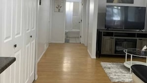 A hallway with wooden flooring, white doors, a sofa, a TV, and a small rug. - FULLY FURNISHED – PERFECT FOR SHORT-TERM OR LONG-TERM RENTALS 
From Jan 1, 2026 (Maple Ridge)