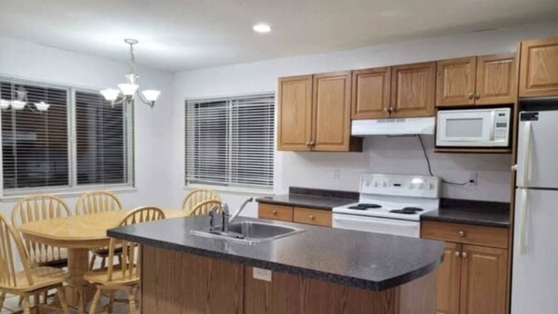 A kitchen with wooden cabinets, a microwave, a stove, and a dining area with chairs and a table. - FULLY FURNISHED – PERFECT FOR SHORT-TERM OR LONG-TERM RENTALS 
From Jan 1, 2026 (Maple Ridge)