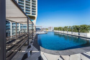 A rooftop pool area with a curved design, sun loungers, and a view of a high-rise building. - Official Mercury Suites With Rooftop Pool Access (St. Julian's)
