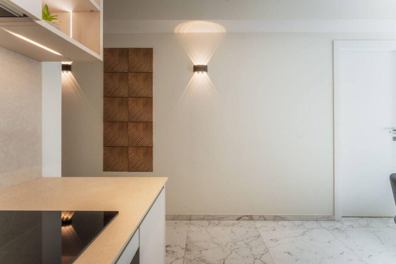 A modern kitchen with a marble countertop and a built-in oven. There is a wooden panel wall and a door in the background.