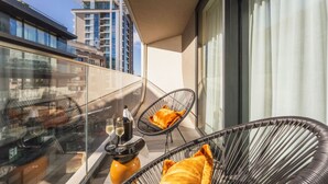 Ein Balkon mit zwei Korbstühlen, einem Glastisch und einer Champagnerflasche.