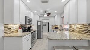 Een moderne keuken met witte kasten, granieten aanrecht en roestvrijstalen apparatuur.