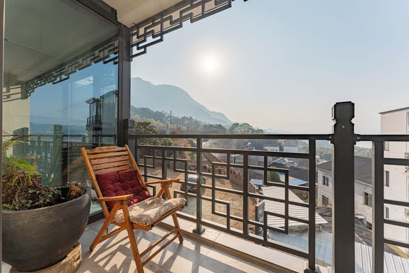 A balcony with a wooden chair, a potted plant, and a view of a mountainous landscape. - Shiyunjian Homestay (Yichang)