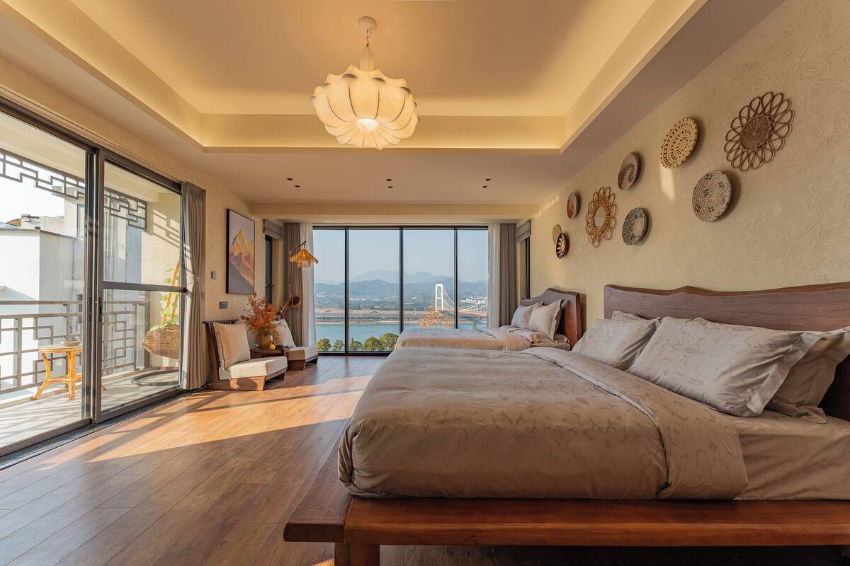 A spacious bedroom with a large bed, a view of a bridge, and a balcony with a wooden table and chairs.