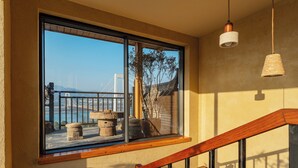 A room with a large window overlooking a bridge and water, a wooden staircase, and a hanging light fixture.