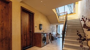 A spacious hallway with a washing machine, a wooden door, and a staircase leading to a balcony.