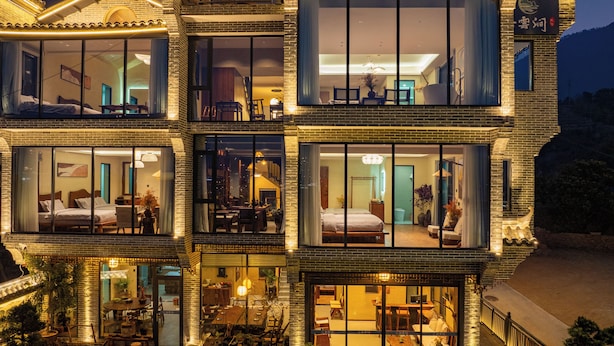 A multi-story hotel with large glass windows, outdoor seating, and a traditional architectural style.