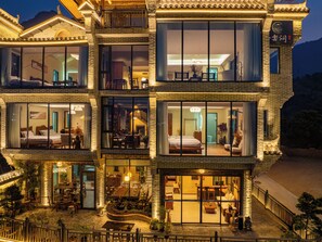 Un hotel a più piani con ampie finestre in vetro, posti a sedere all'aperto e uno stile architettonico tradizionale.