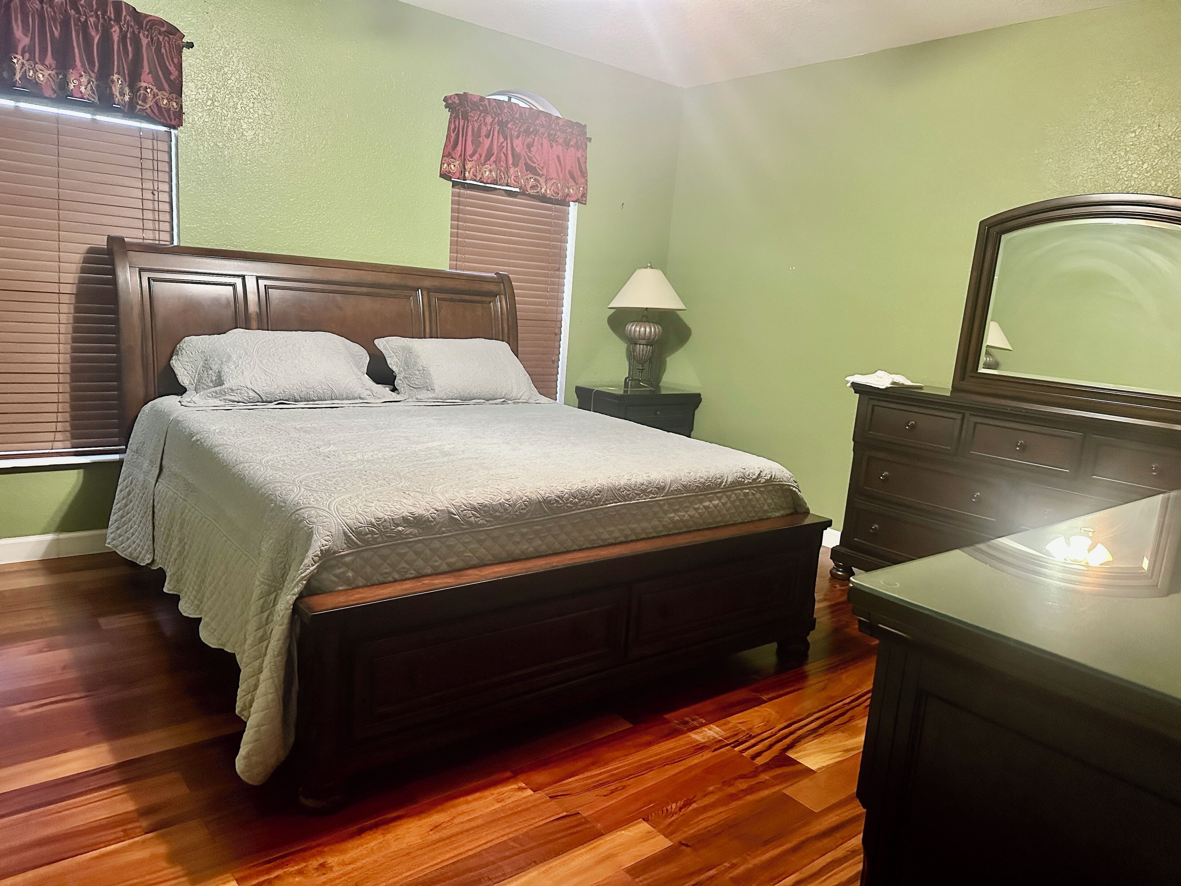 A bedroom with a wooden bed, a nightstand with a lamp, and a dresser.