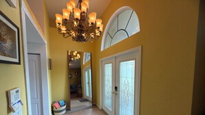 A hallway with a chandelier, a welcome mat, and a door with frosted glass panels.