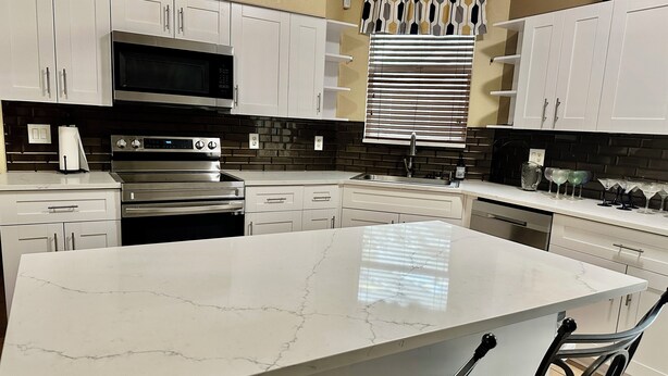 A modern kitchen with white cabinets, a large island, stainless steel appliances, and a brick backsplash.