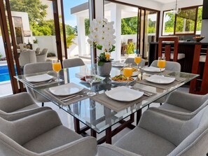 A dining area with a glass table, chairs, and a view of a pool and greenery.