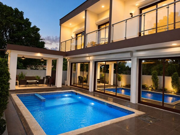 A modern two-story house with a swimming pool, outdoor seating, and large windows.
