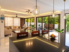 A modern living room with a glass-top coffee table, beige sofas, and a dining area with a glass-top table.