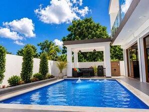 A swimming pool with a patio area, a barbecue grill, and a covered seating area.