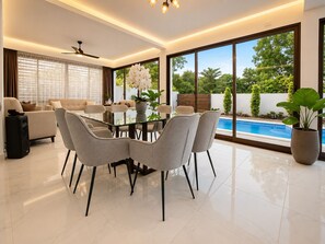 A modern living room with a glass dining table, sofas, and a view of a swimming pool.
