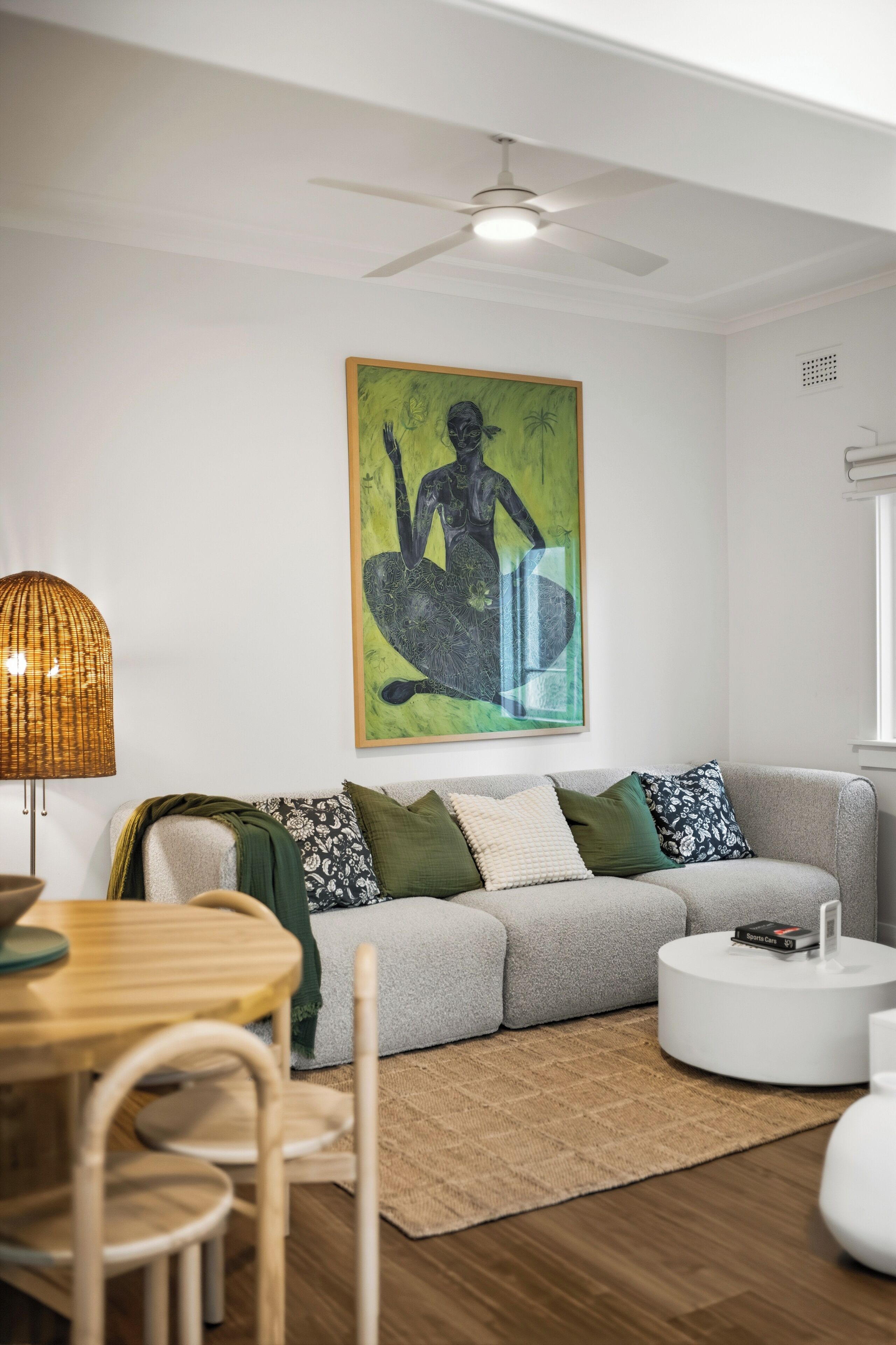 A modern living room with a grey sofa, a round coffee table, a dining table with chairs, a floor lamp, and a ceiling fan.