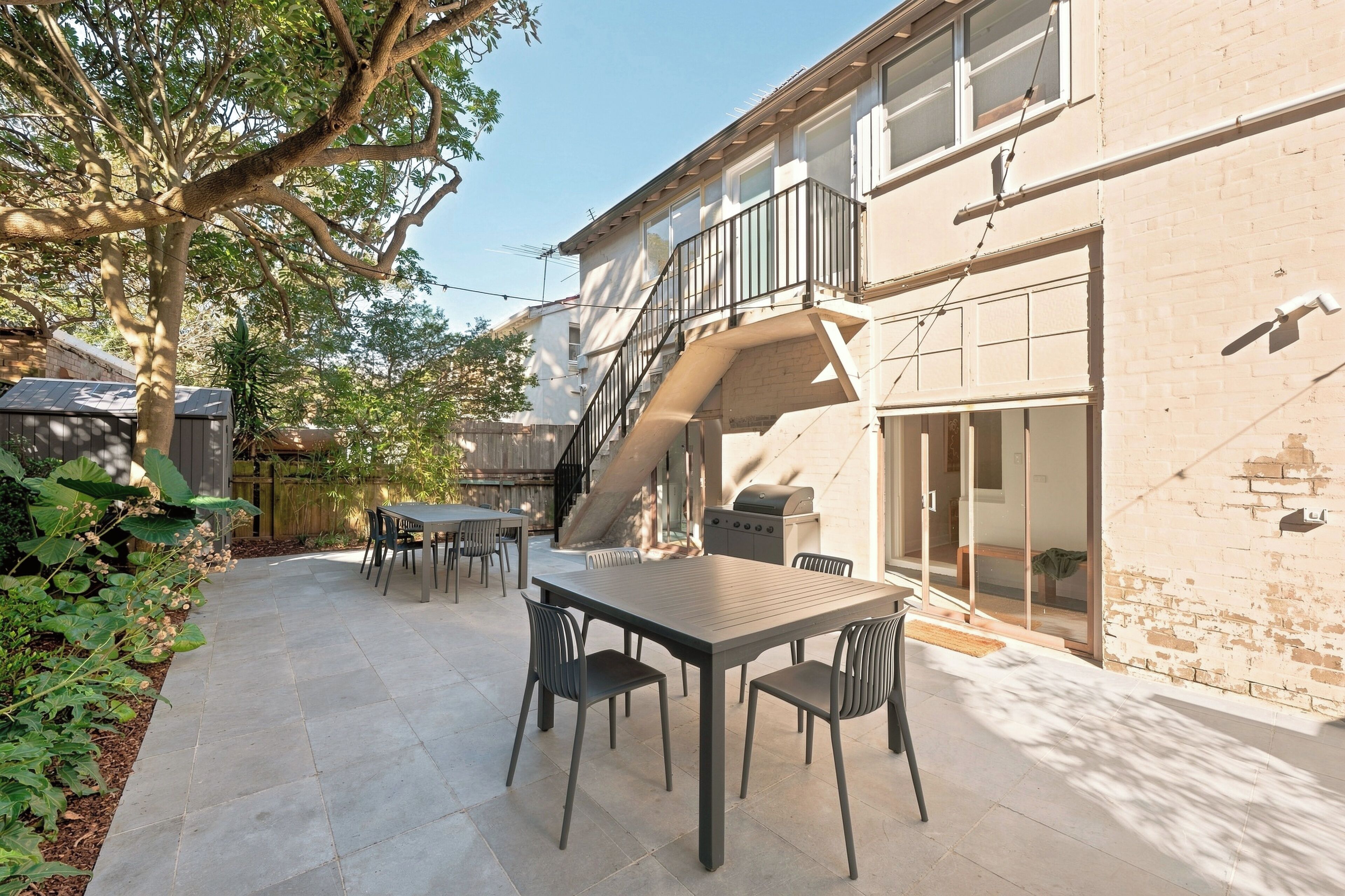 Un patio exterior con mesa y sillas, una parrilla y una escalera que lleva a un nivel superior.
