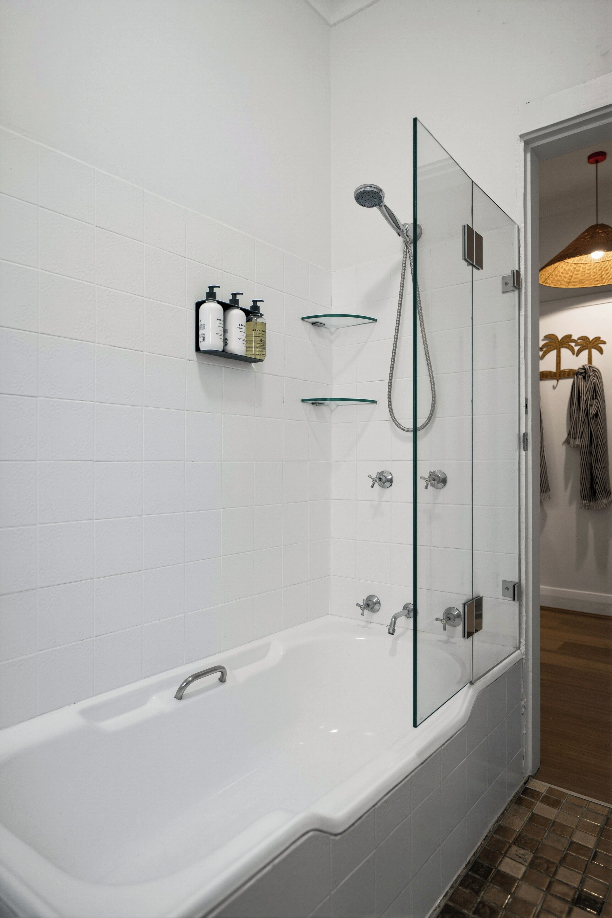 A modern bathroom with a glass-enclosed shower, a white bathtub, and a shelf with toiletries.