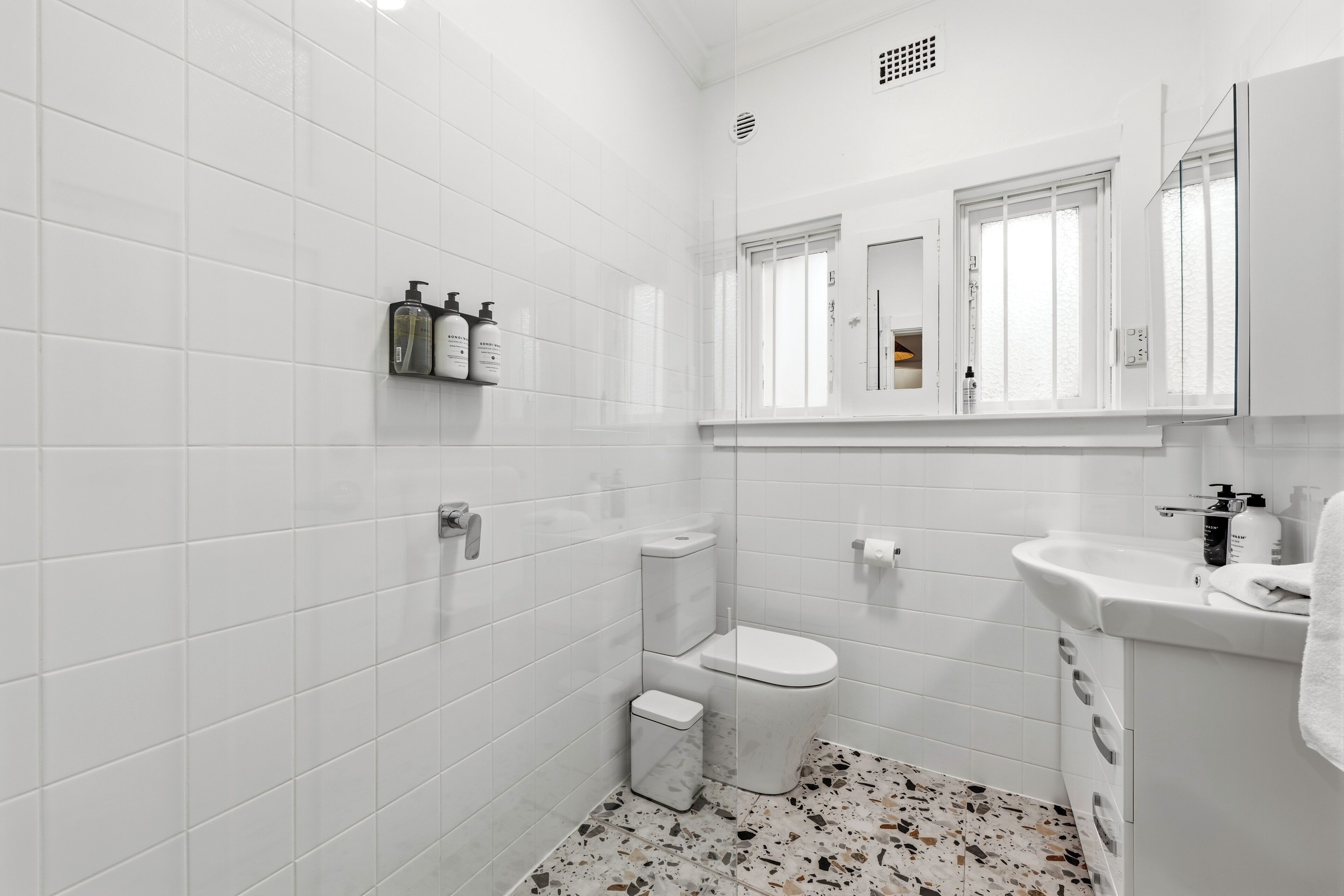 A modern bathroom with white tiles, a toilet, a sink, and a mirror.