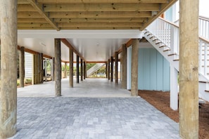 A covered outdoor area with a wooden ceiling, stone flooring, and a staircase leading to an upper level.