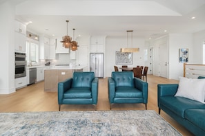 A spacious living area with a kitchen, two blue leather chairs, a teal sofa, and a patterned rug.