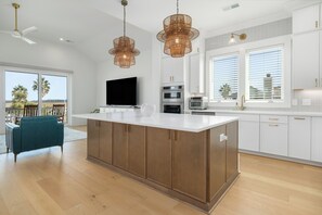 A modern kitchen with a large island, white cabinetry, stainless steel appliances, and pendant lighting.