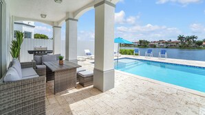 Ein überdachter Außenbereich mit Pool, Korbmöbeln und Grill.