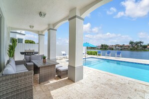 Un espace extérieur abrité comprenant une piscine, des meubles en osier et un barbecue.