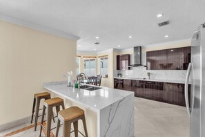 Une cuisine moderne dotée d’un îlot en marbre, de meubles de rangement en bois foncé et d’un réfrigérateur en acier inoxydable.