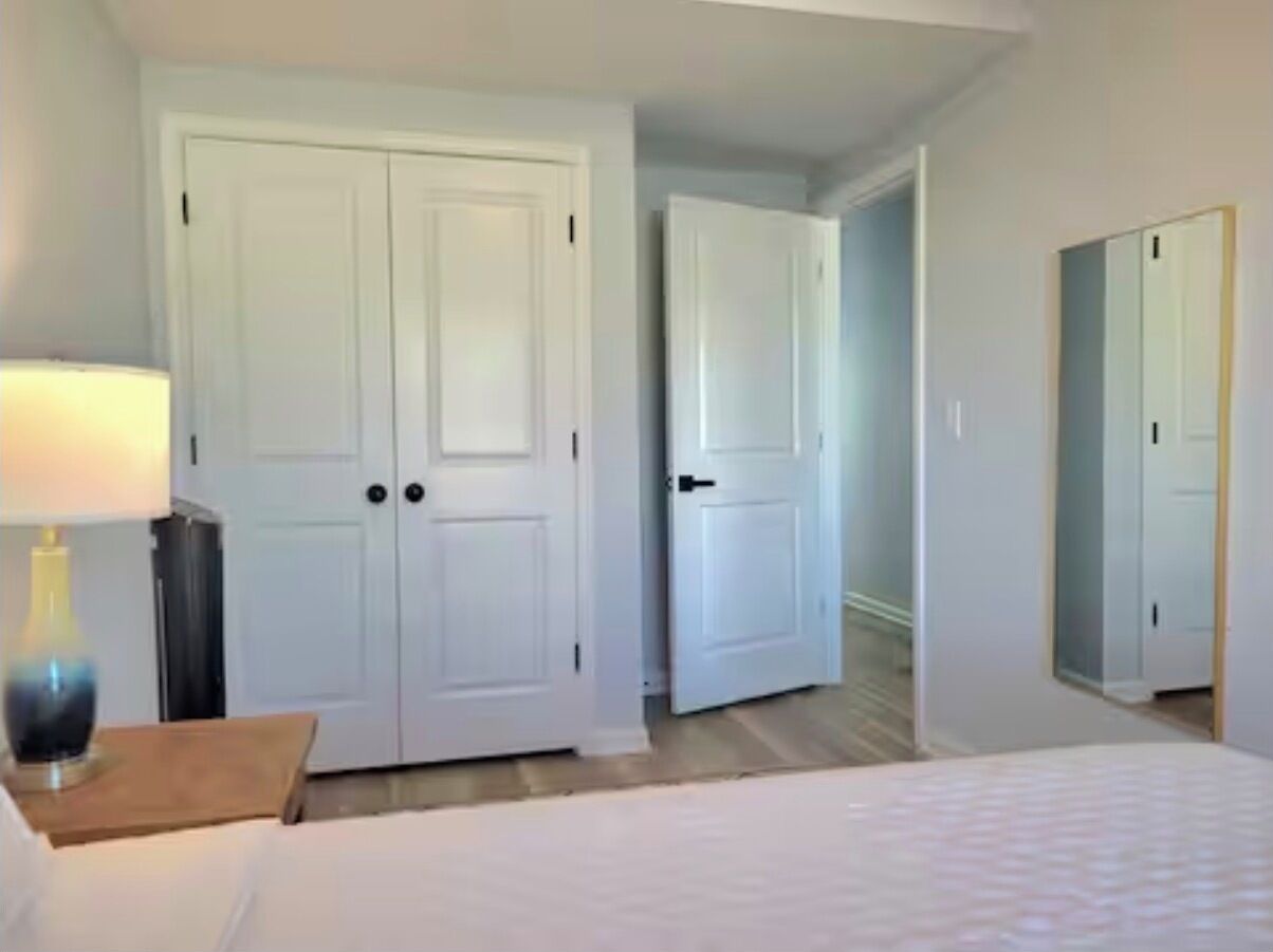 Een hotelkamer met een bed, nachtkastje, lamp en twee witte deuren.