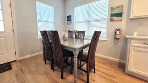 Un comedor con una mesa rectangular y cuatro sillas, una puerta blanca y un ventanal con persianas.