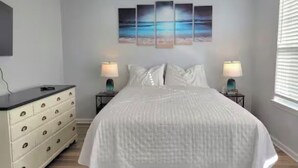 Un dormitorio con cama, mesitas de noche, cómoda y una obra de arte colgada en la pared.