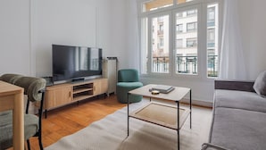 En moderne stue med et fladskærms-tv, et tv-møbel i træ, en turkis lænestol og en grå sofa.