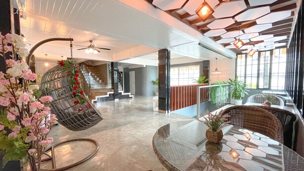 A spacious lobby with a high ceiling, a hanging chair with flowers, a round glass table, and a staircase leading to upper floors. - Le Cartier Guesthouse (Patong)