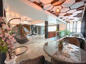 Een ruime lobby met een hoge plafond, een hangstoel met bloemen, een ronde glazen tafel en een trap naar de verdiepingen erboven.