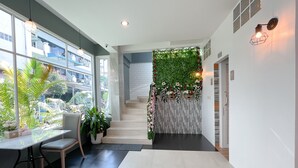 A modern hotel lobby with a staircase, indoor plants, and a view of the outside. - Le Cartier Guesthouse (Patong)