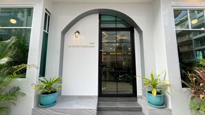 The entrance of Le Cartier Guesthouse with a black door, white walls, and two potted plants on either side. - Le Cartier Guesthouse (Patong)